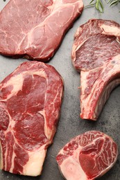 Photo of Pieces of raw beef meat and rosemary on grey table, flat lay