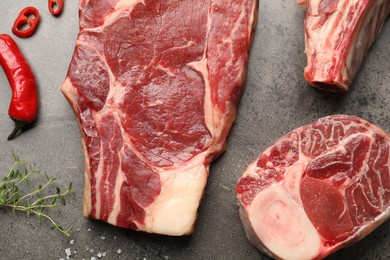 Photo of Pieces of raw beef meat and spices on grey table, flat lay
