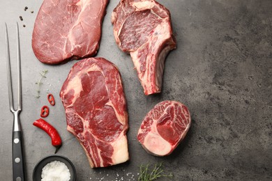 Photo of Pieces of raw beef meat, spices and carving fork on grey table, flat lay. Space for text