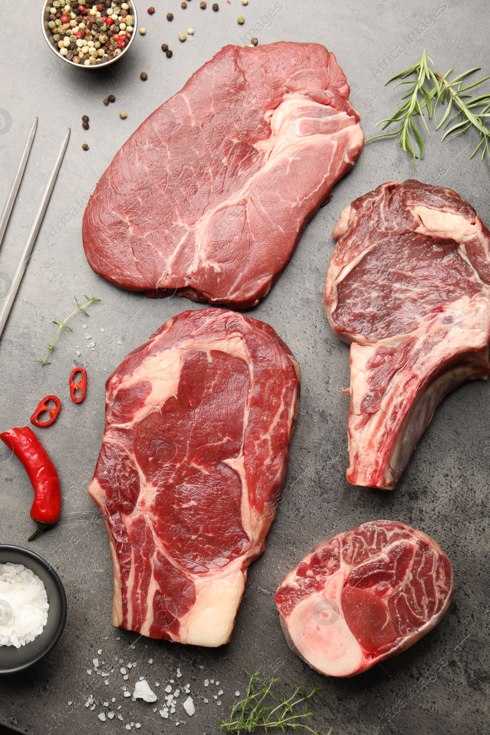 Pieces of raw beef meat, spices and carving fork on grey table, flat lay Photo of Pieces of raw beef meat, spices and carving fork on grey table, flat lay