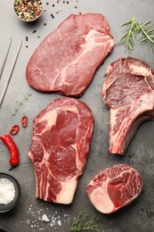Photo of Pieces of raw beef meat, spices and carving fork on grey table, flat lay