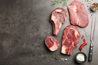 Photo of Pieces of raw beef meat, spices and carving fork on grey table, flat lay. Space for text