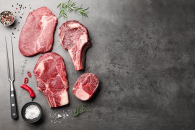 Photo of Pieces of raw beef meat, spices and carving fork on grey table, flat lay. Space for text