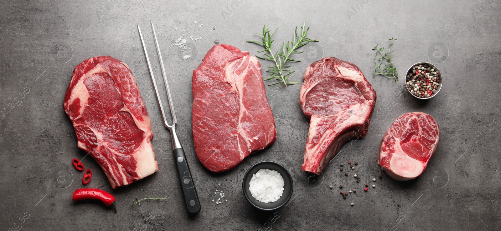 Pieces of raw beef meat, spices and carving fork on grey table, flat lay Photo of Pieces of raw beef meat, spices and carving fork on grey table, flat lay