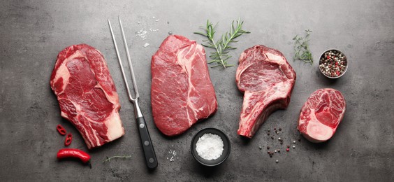 Photo of Pieces of raw beef meat, spices and carving fork on grey table, flat lay