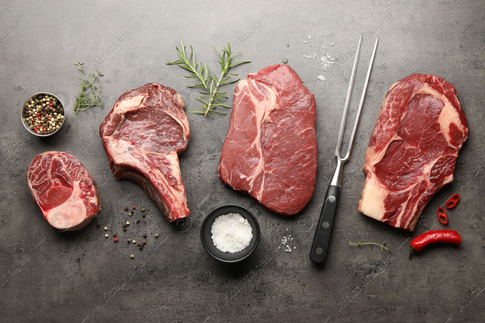 Pieces of raw beef meat, spices and carving fork on grey table, flat lay Photo of Pieces of raw beef meat, spices and carving fork on grey table, flat lay