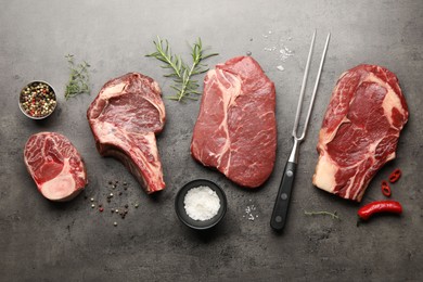 Photo of Pieces of raw beef meat, spices and carving fork on grey table, flat lay