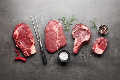 Photo of Pieces of raw beef meat, spices and carving fork on grey table, flat lay