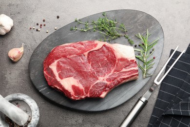 Photo of Piece of raw beef meat, spices and carving fork on grey table, flat lay