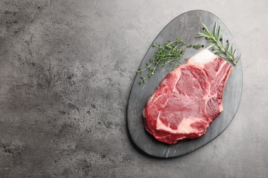 Photo of Piece of raw beef meat and spices on grey table, top view. Space for text