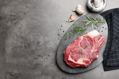 Photo of Piece of raw beef meat, spices, mortar and pestle on grey table, flat lay. Space for text