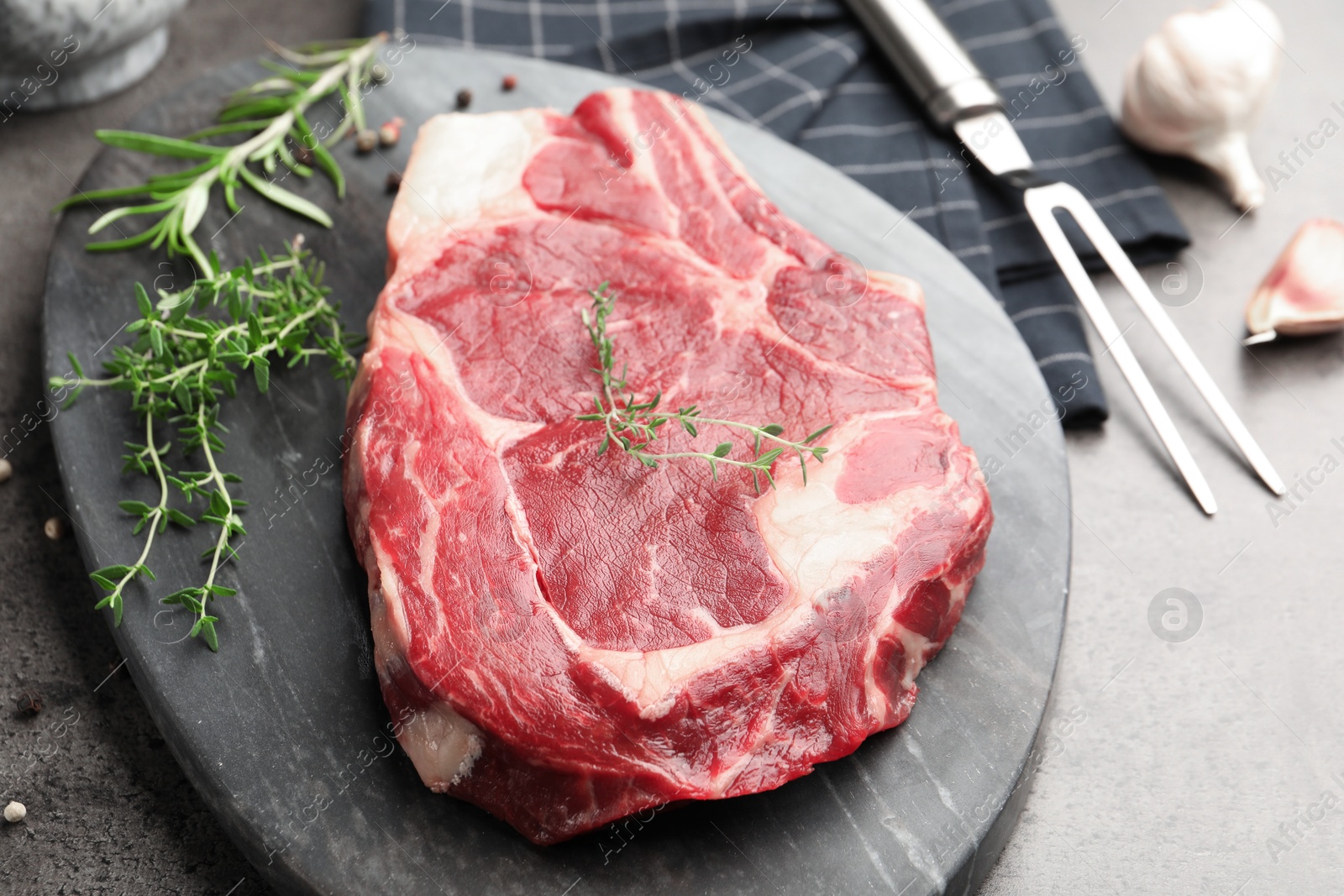 Photo of Piece of raw beef meat, spices and carving fork on grey table, closeup