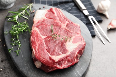 Photo of Piece of raw beef meat, spices and carving fork on grey table, closeup