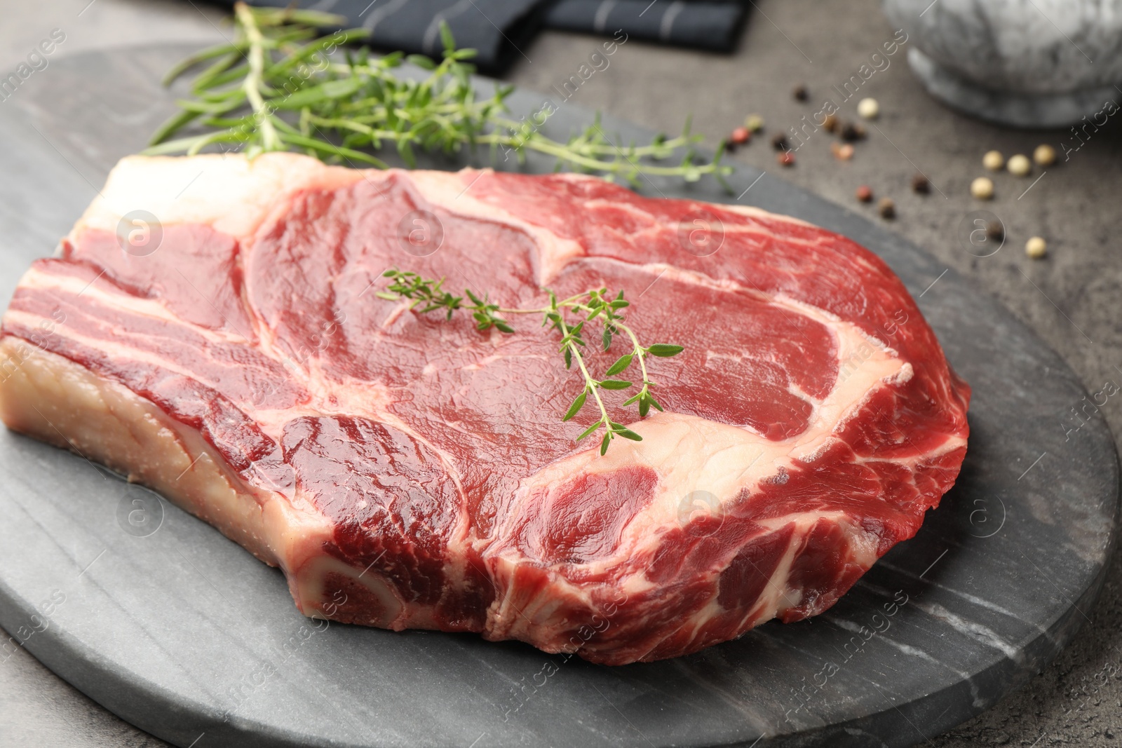 Photo of Piece of raw beef meat and spices on grey table, closeup