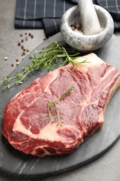 Photo of Piece of raw beef meat, spices, mortar and pestle on grey table, closeup
