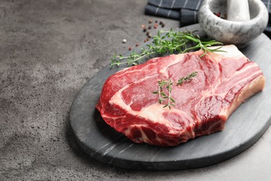 Photo of Piece of raw beef meat, spices, mortar and pestle on grey table, closeup. Space for text