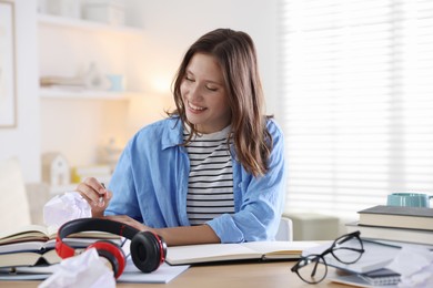 Photo of Smiling student with pen and books preparing for exam at table indoors