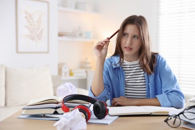 Photo of Worried student with books and pen preparing for exam at table indoors. Space for text