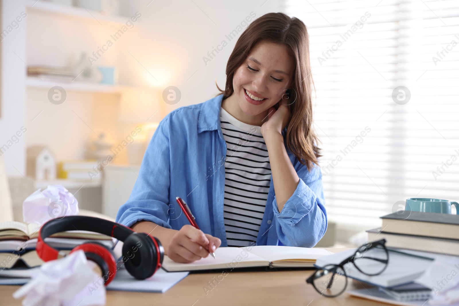 Photo of Smiling student with pen and books preparing for exam at table indoors