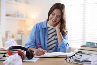 Photo of Smiling student with pen and books preparing for exam at table indoors