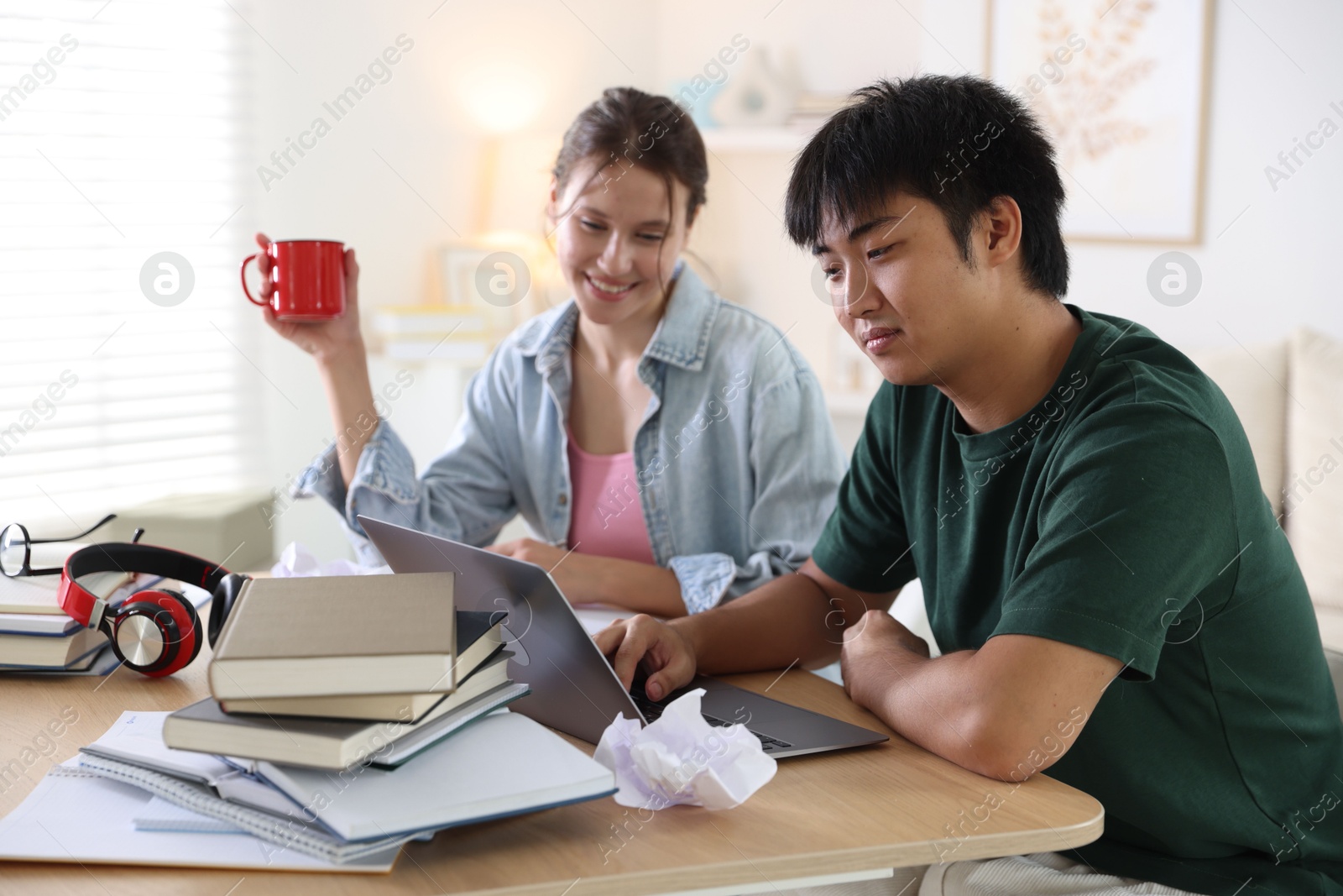 Photo of Students with books and laptop preparing for exam at wooden table indoors