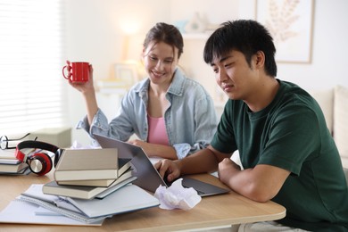 Photo of Students with books and laptop preparing for exam at wooden table indoors