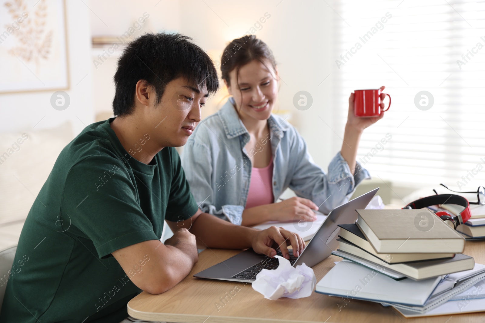 Photo of Students with books and laptop preparing for exam at wooden table indoors