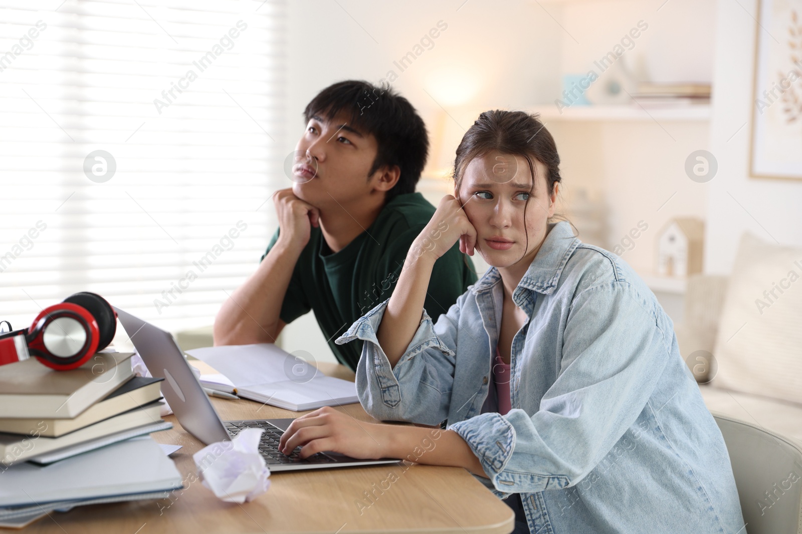 Photo of Worried students with books and laptop preparing for exam at wooden table indoors
