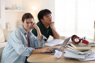 Photo of Worried students with books and laptop preparing for exam at wooden table indoors