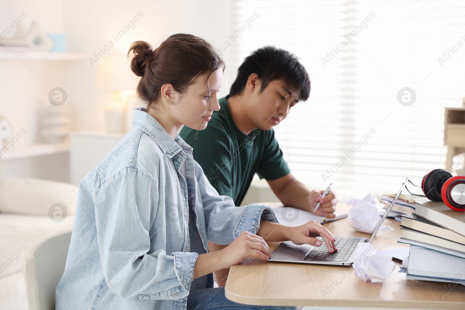 Photo of Students with books and laptop preparing for exam at wooden table indoors