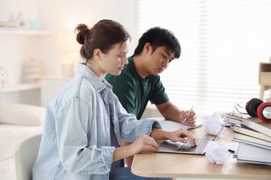 Photo of Students with books and laptop preparing for exam at wooden table indoors