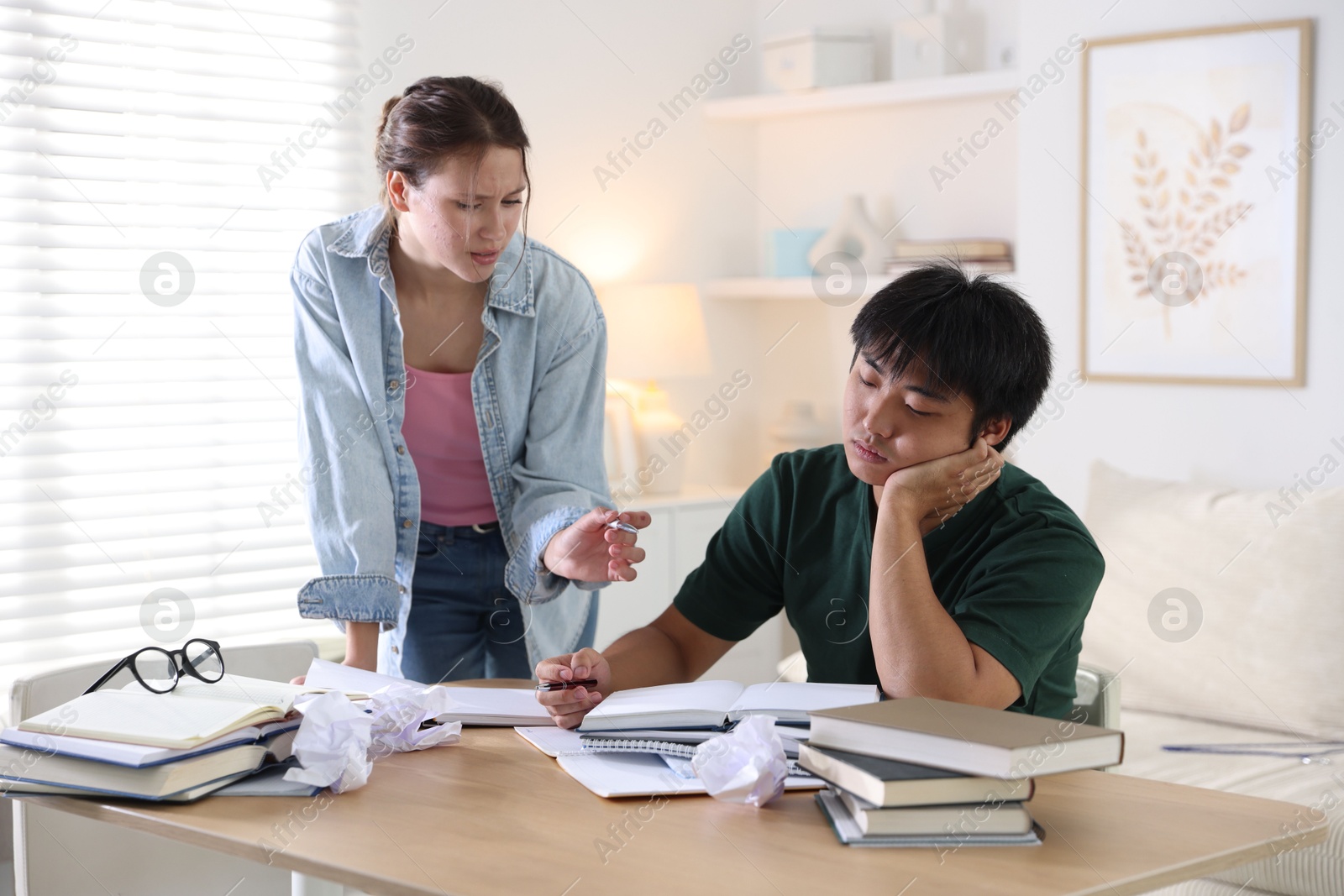 Photo of Tired students with books preparing for exam at wooden table indoors