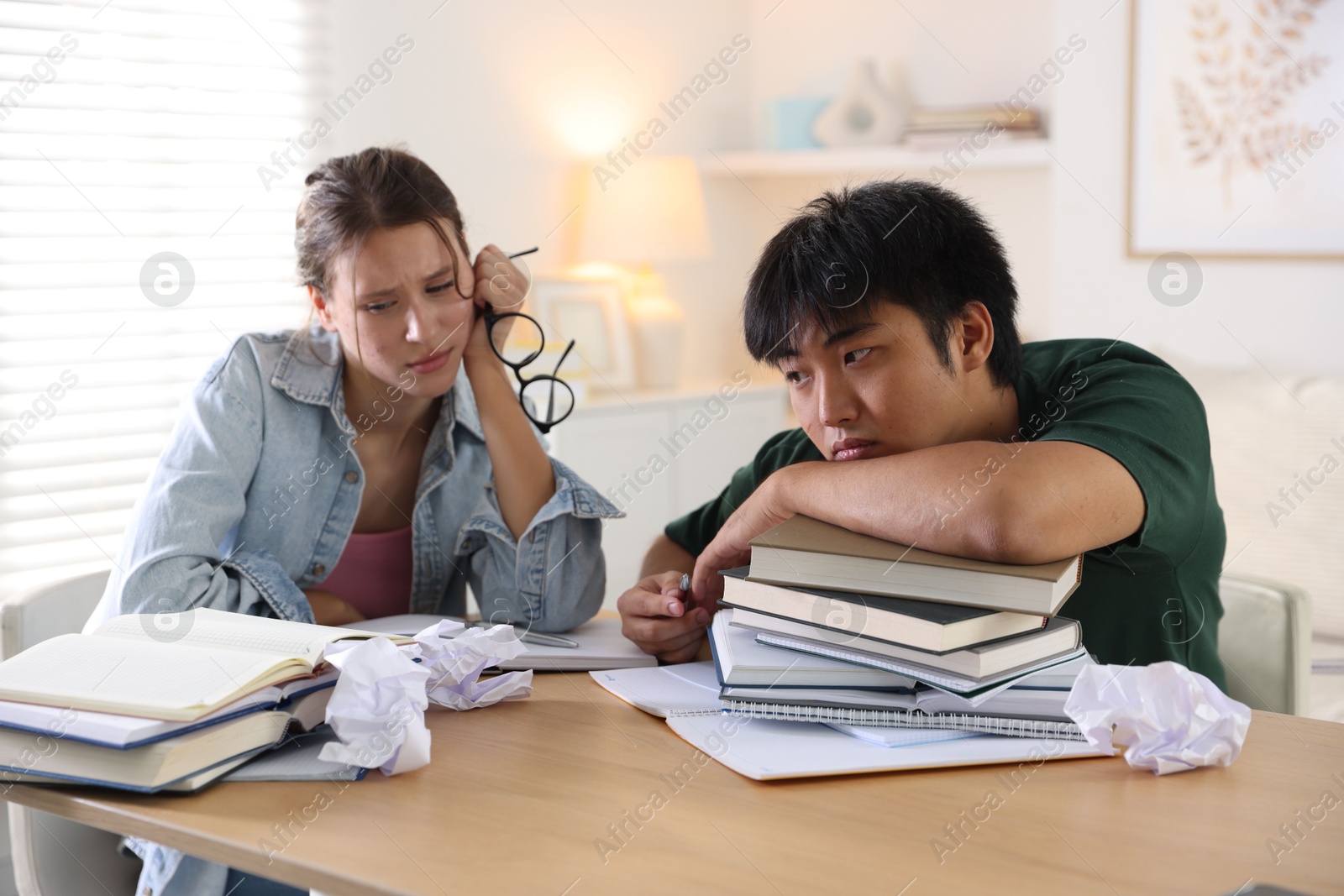 Photo of Tired students with books preparing for exam at wooden table indoors