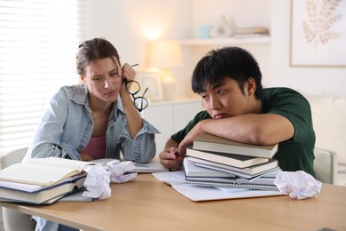 Photo of Tired students with books preparing for exam at wooden table indoors