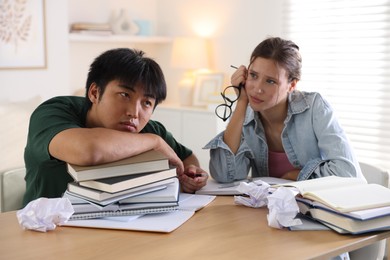 Photo of Tired students with books preparing for exam at wooden table indoors