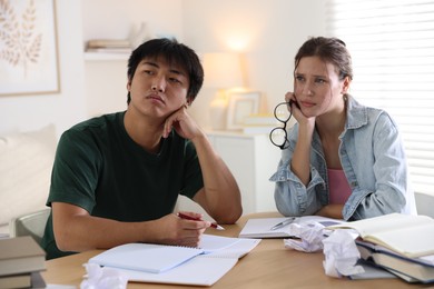 Photo of Tired students with books preparing for exam at wooden table indoors