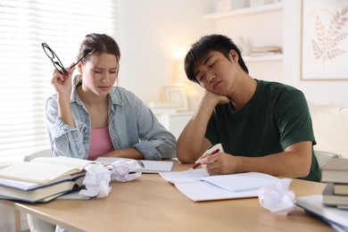 Photo of Tired students with books preparing for exam at wooden table indoors