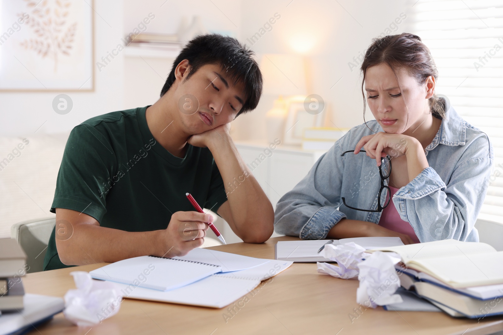 Photo of Tired students with books preparing for exam at wooden table indoors
