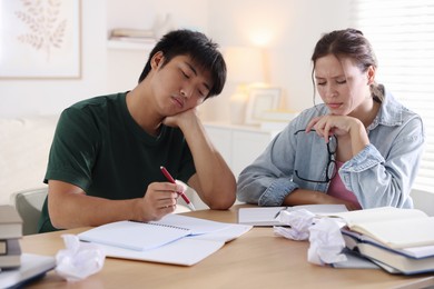 Photo of Tired students with books preparing for exam at wooden table indoors
