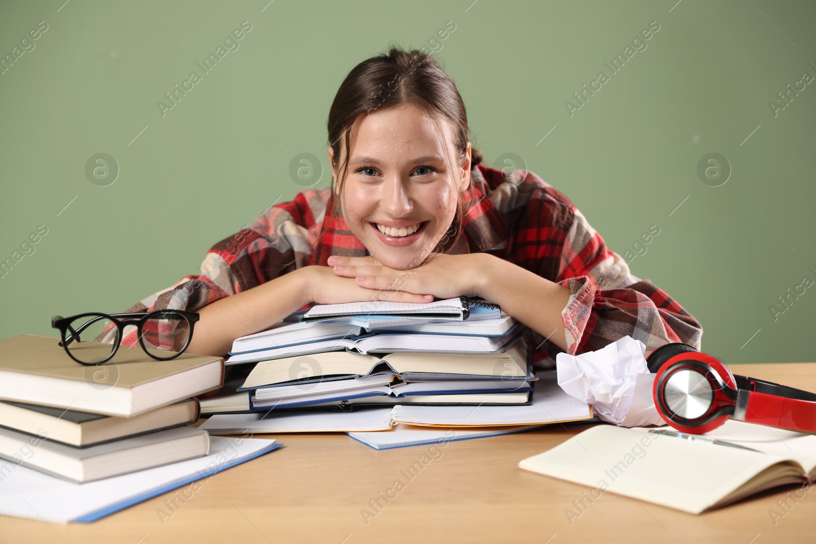 Photo of Portrait of smiling student with books preparing for exam at wooden table near green wall