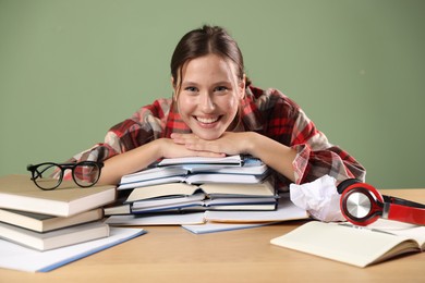 Photo of Portrait of smiling student with books preparing for exam at wooden table near green wall