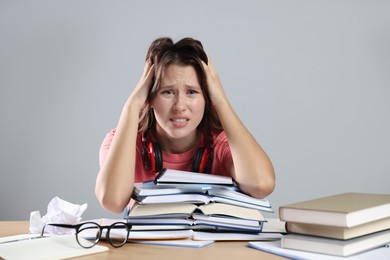 Photo of Worried student with books preparing for exam at table near grey wall