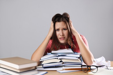 Photo of Worried student with books preparing for exam at table near grey wall