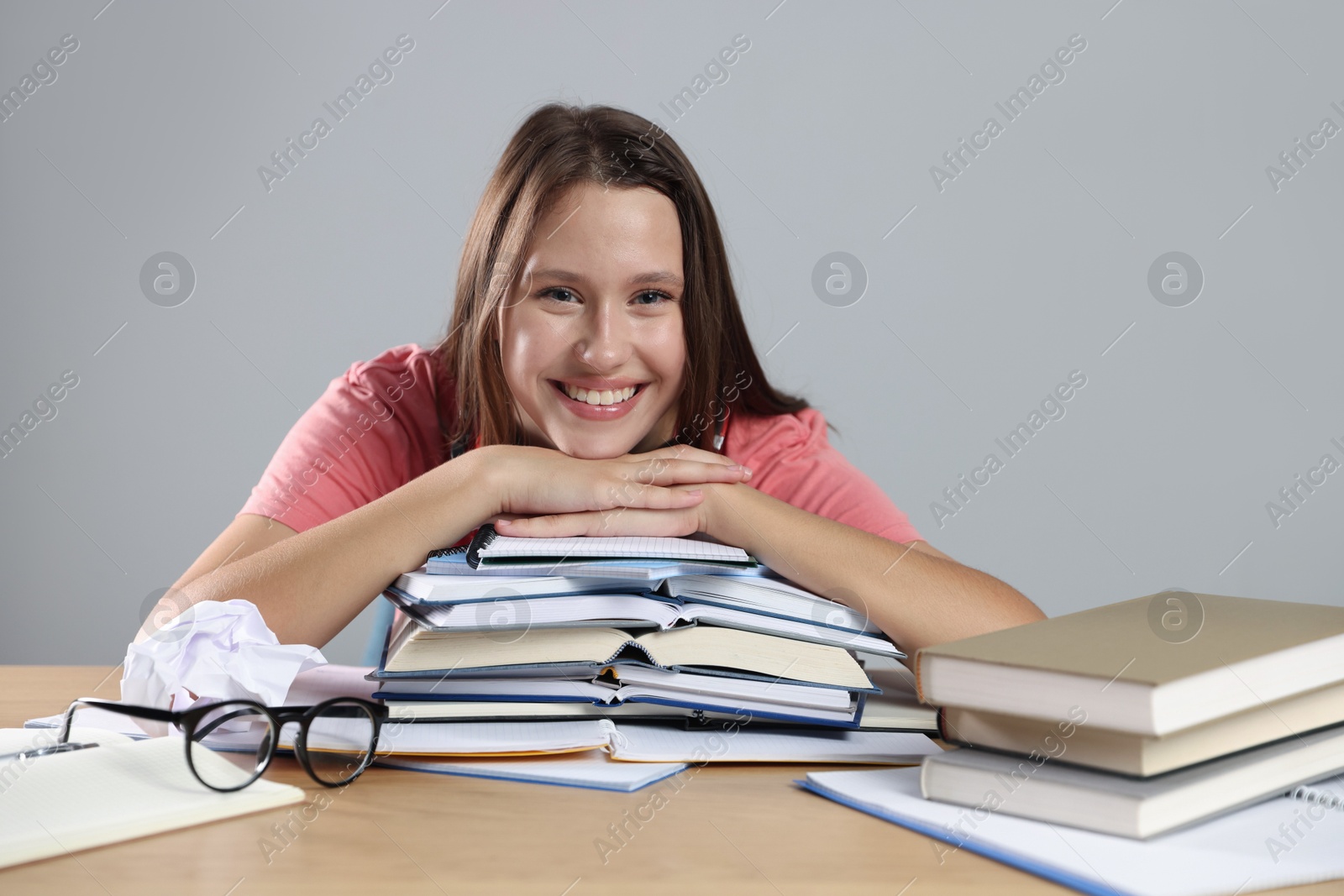 Photo of Smiling student with books preparing for exam at wooden table near grey wall