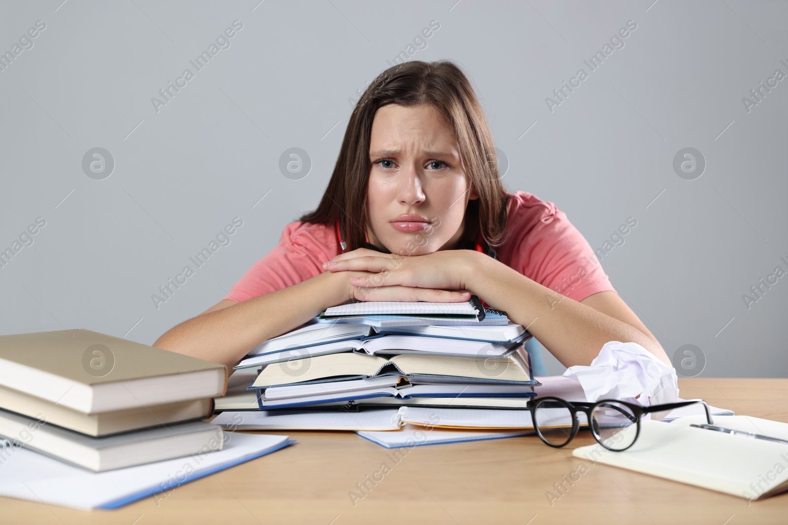 Photo of Tired student with books preparing for exam at wooden table near grey wall