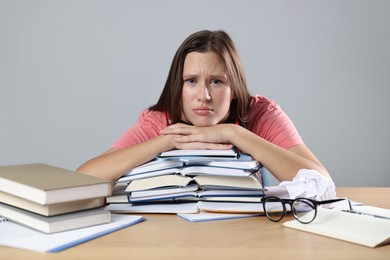 Photo of Tired student with books preparing for exam at wooden table near grey wall