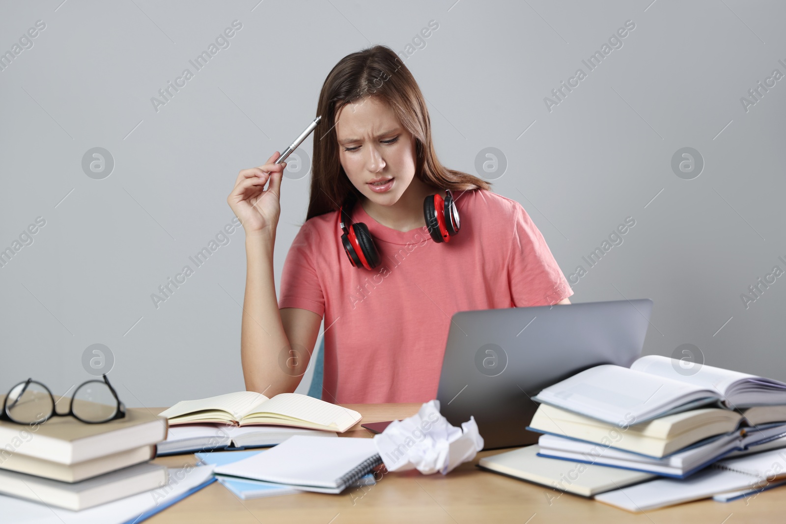 Photo of Tired student with laptop, pen and books preparing for exam at table near grey wall