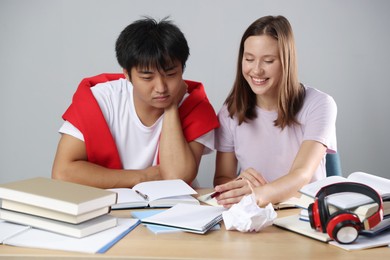 Photo of Happy students with books preparing for exam at table near grey wall