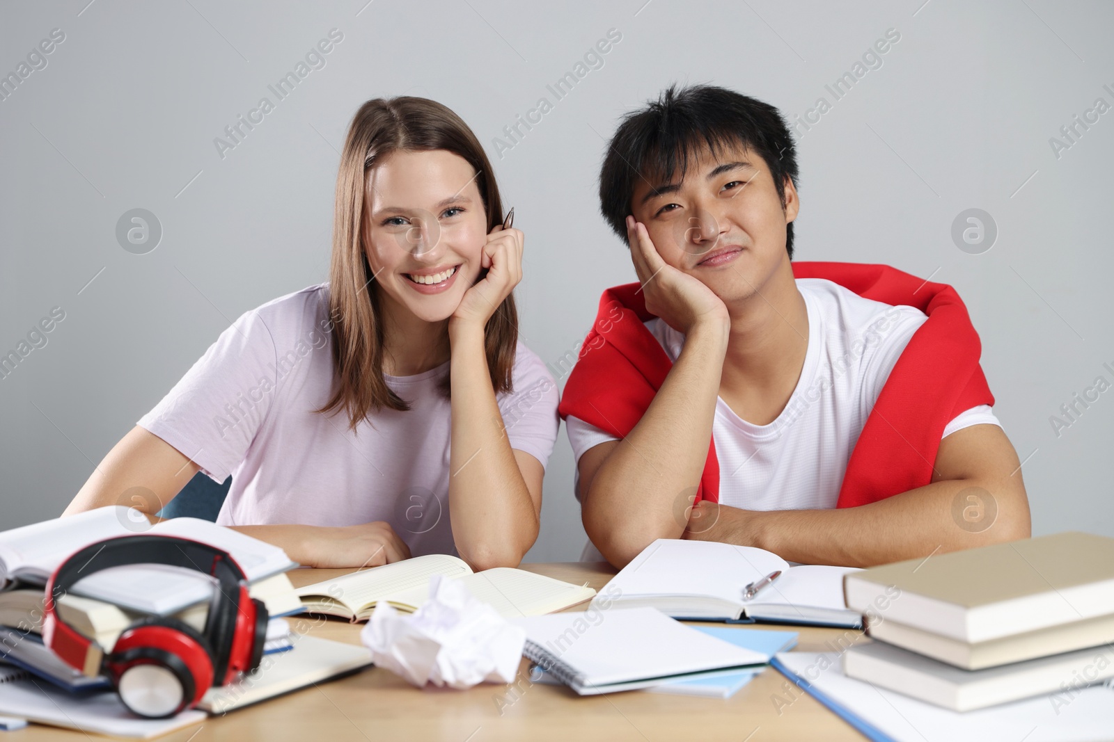 Photo of Happy students with books preparing for exam at table near grey wall