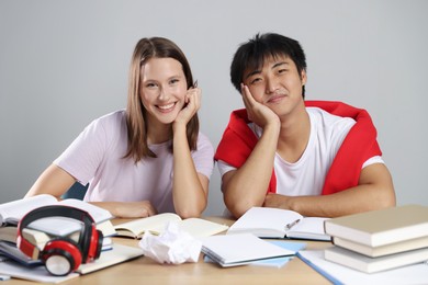 Photo of Happy students with books preparing for exam at table near grey wall